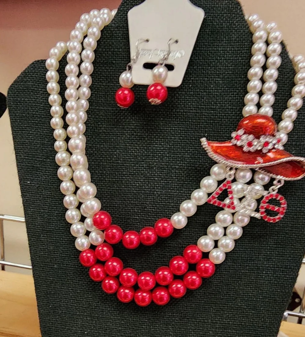 Red and white layered pearl necklace with matching red drop earrings and a red hat ΔΣΘ brooch