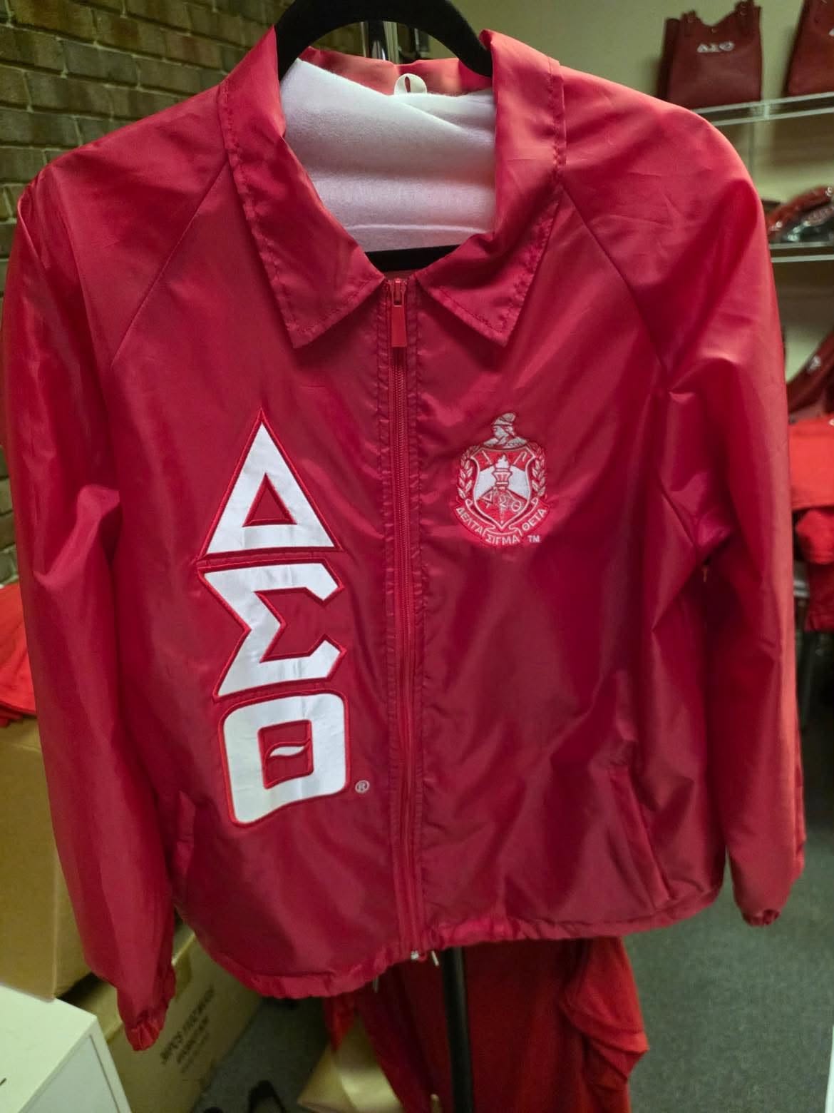 Red DST line jacket with vertical white ΔΣΘ symbols and the Sorority crest, shown on a hanger