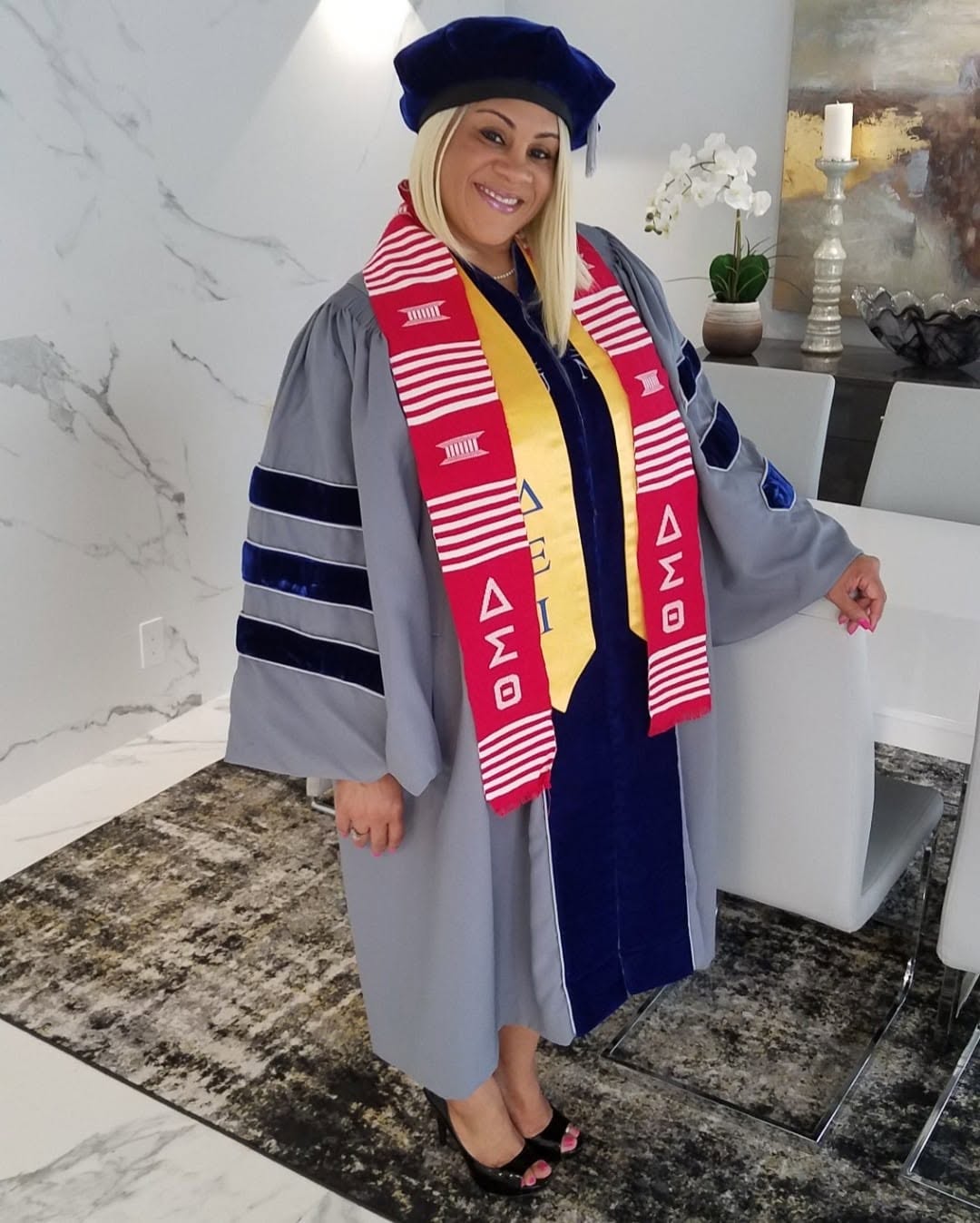 Delta soror in doctoral cap and gown wearing a crimson and white ΔΣΘ kente graduation stole